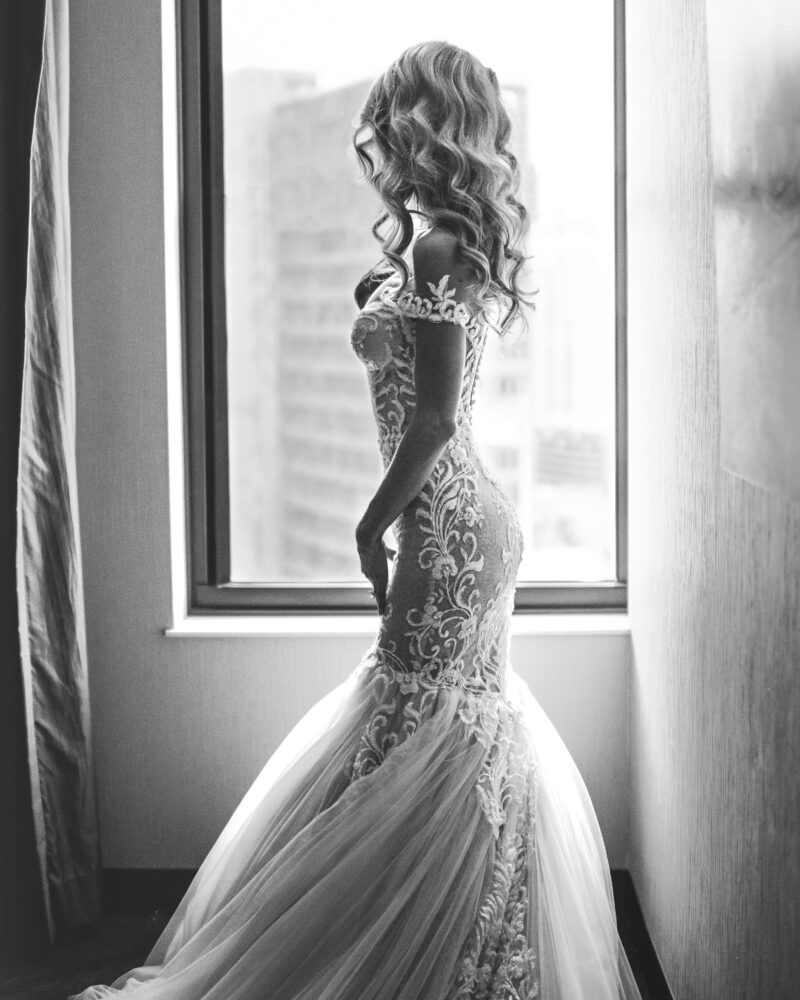 Bride by window. Hands on legs looking into sunset