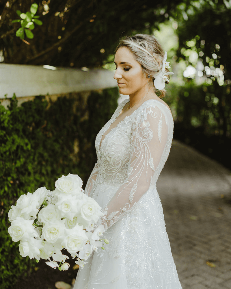 bride looking down in garden. Bride wears long sleeve a-line gown while holding bouquet