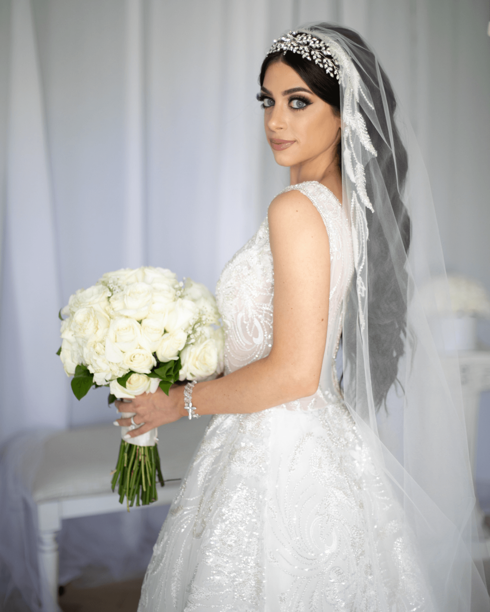 Bride Sara Manor looking over her shoulder while holding a bouquet of white roses.